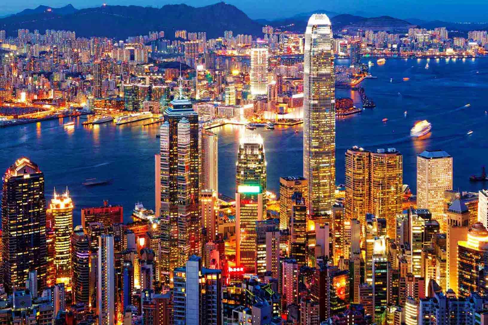 Hong Kong Visa Hong Kong skyline at dusk with illuminated skyscrapers, Victoria Harbour, and mountains in background